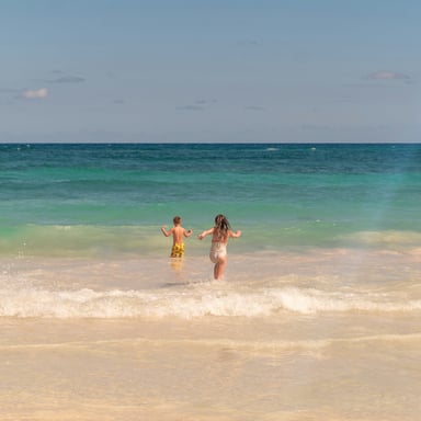 Two kids running into turquoise waves on white sand beach